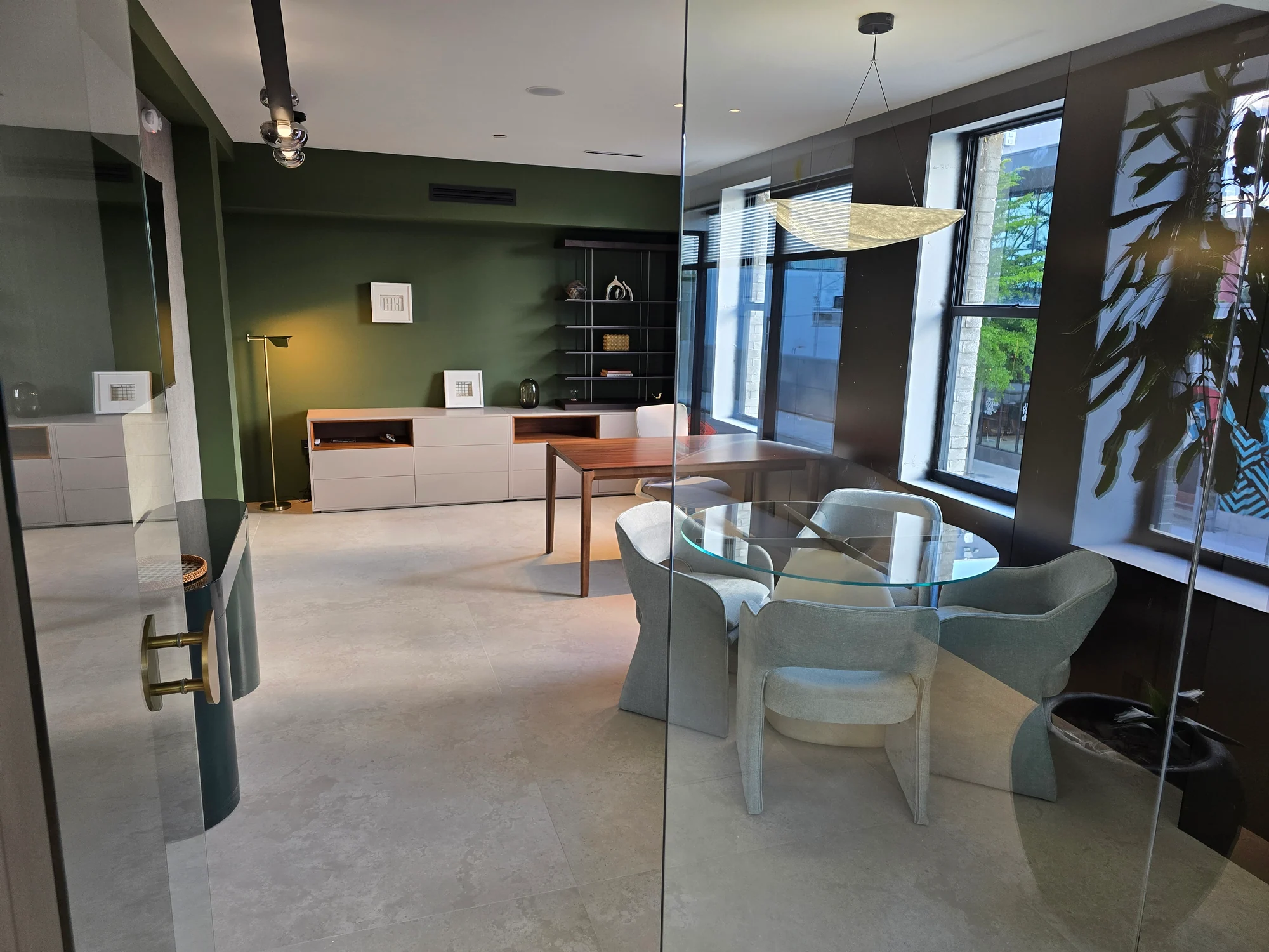 A room with a round glass table, upholstered chairs, a desk and green walls.