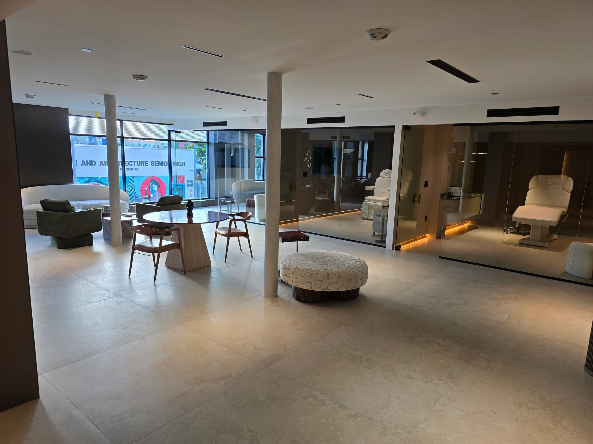 Světlý lounge se stoly, židlemi a prosklenými místnostmi s bílými polohovacími křesly.