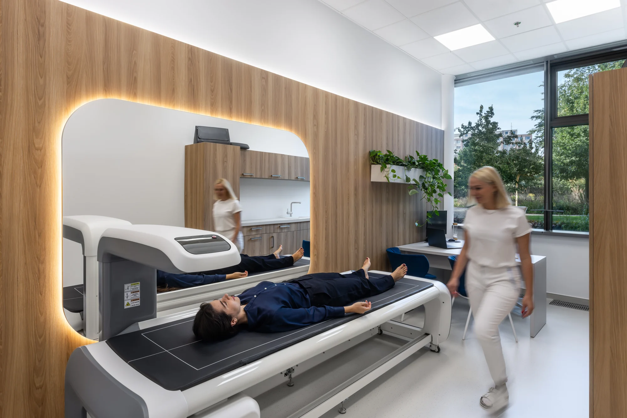 Žena ležící na vyšetřovacím stole a žena v bílém oděvu ve světlé místnosti kliniky.